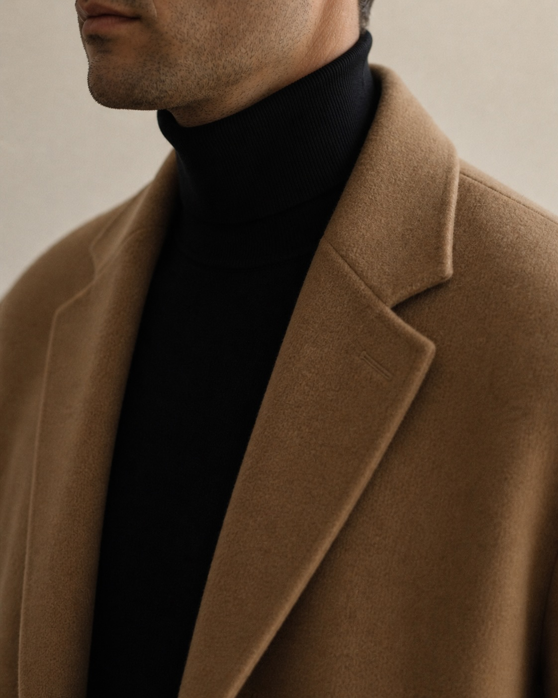 Chest-up close-crop, a man in a black turtleneck under a camel topcoat.