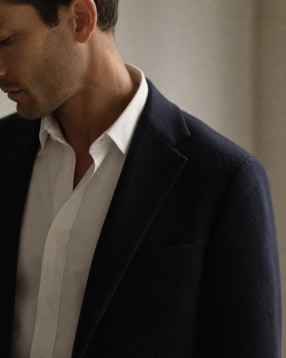 Profile of a man, ink-navy blazer over white oxford, head turned down.